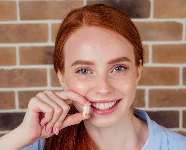 smiling woman holding a tooth in front of her face