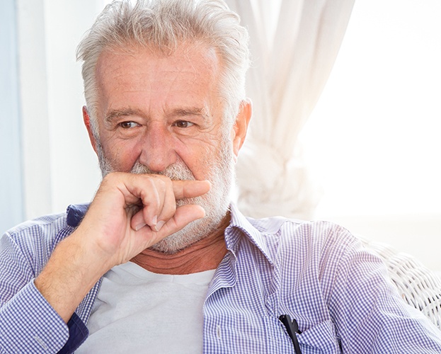 Older man in need of dentures covering his mouth