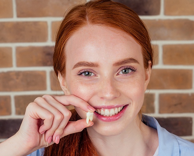Woman smiling and holding her extracted tooth