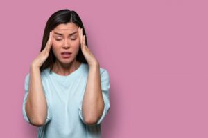 woman holding her head with worry in front of a pink background