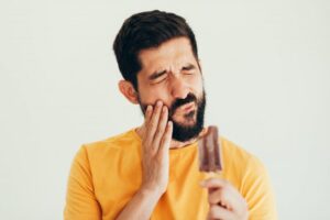 man holding his face and popsicle with tooth sensitivity