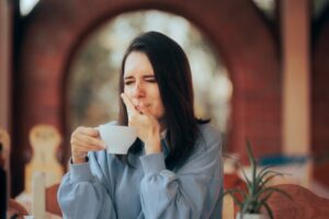 woman holding her sensitive mouth and a coffee cup