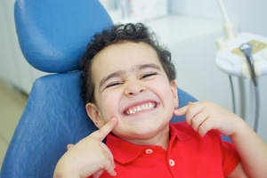 Little boy in dental chair pointing to his smile